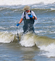 photo of a man walking through 
the surf with water sampling equipment