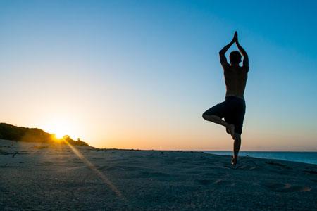 Man practicing yoga on a clear, clean beach