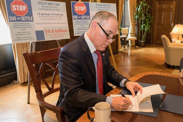 photo of EPA Administrator signing S&S memo and directive, with placards in the background "Stop Sue and Settle"