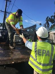 EPA worker hands household waste to another EPA worker in a truck