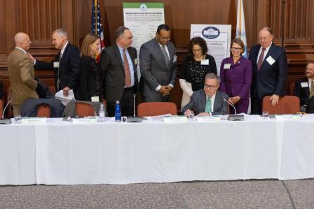 Acting Administrator Wheeler seated at a long table signing a paper with onlookers