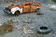 Photo: car in a junkyard with old tires laying on the ground nearby.