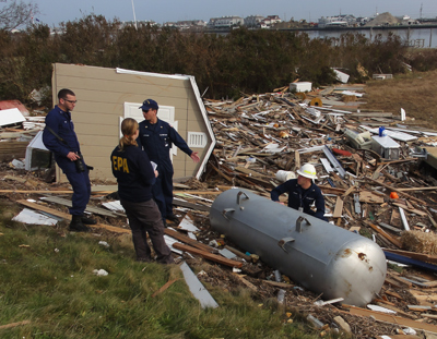 three uniformed people standing next to a large pile of building debris and one large steel tank lying on the ground