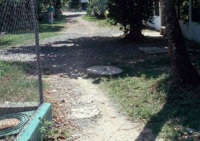 The photo shows a covered manhole off to the side of a path in a residential area.