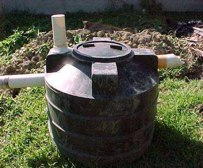 The photo shows a septic tank sitting above ground in a grassy area.