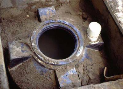 The photo shows a top view of an open septic tank set in the ground. 