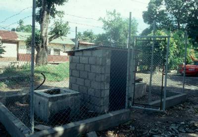 The photo shows a small shelter built of concrete blocks and surrounded by a high mesh fence with a barbed wire top.