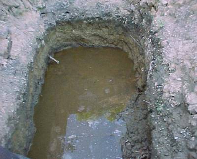 The photo shows water in a shallow dug hole in the ground.