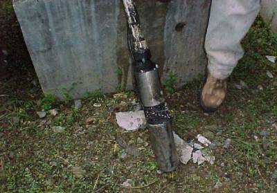 The photo shows a dirty pump leaning on the ground and held on one end by a person.