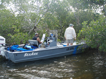 researchers in grey boat nosed up to red mangrove trees.