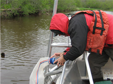 sampler leaning over side of boat in river deploying miller sampler.