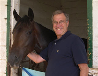 Portrait of Paul Giardina next to a dark brown horse.