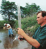 Two men monitoring water quality in a stream.